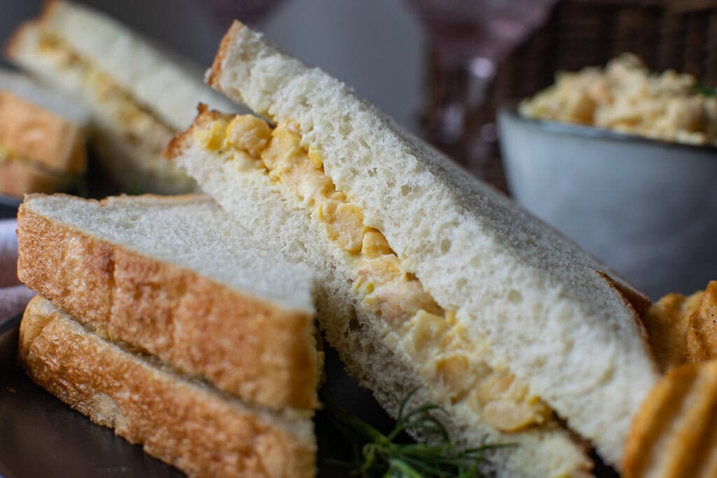 A close up of a chickpea dill salad sandwich slice in half.