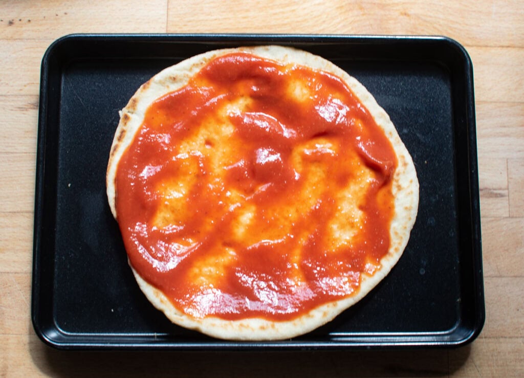 A Naan bread covered in tomato sauce on a baking sheet.