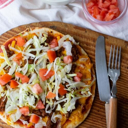 A taco pizza made on Naan bread and topped with fresh shredded lettuce and diced tomatoes.
