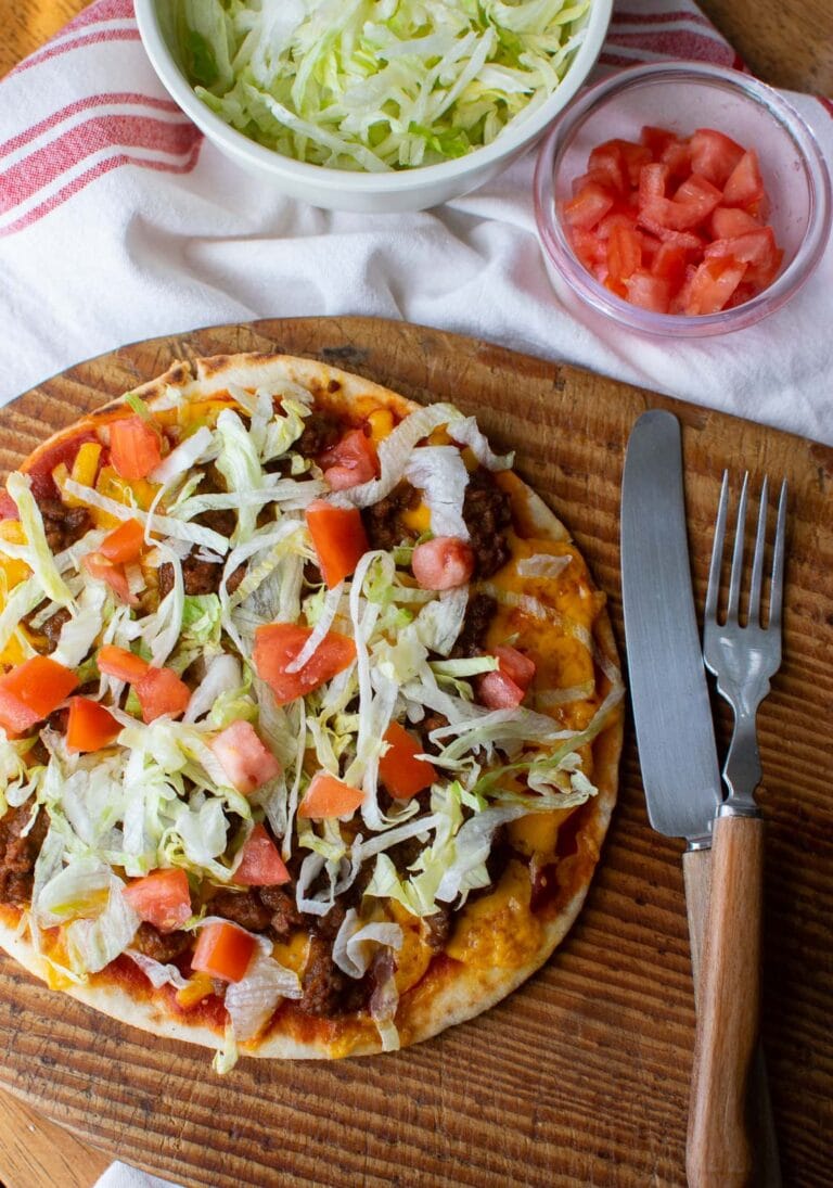 A taco pizza made on Naan bread and topped with fresh shredded lettuce and diced tomatoes.
