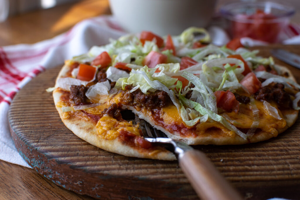 A taco pizza mad on Naan bread and topped with fresh lettuce and tomato.