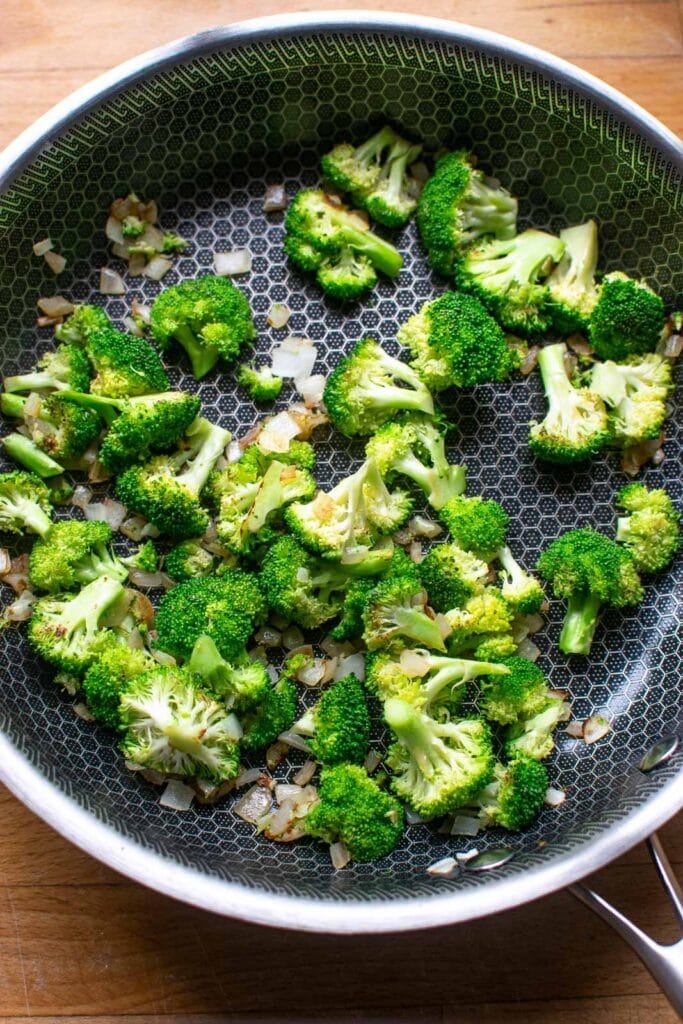 Chopped fresh broccoli and diced onions in a frying pan that have been sautéed lightly.