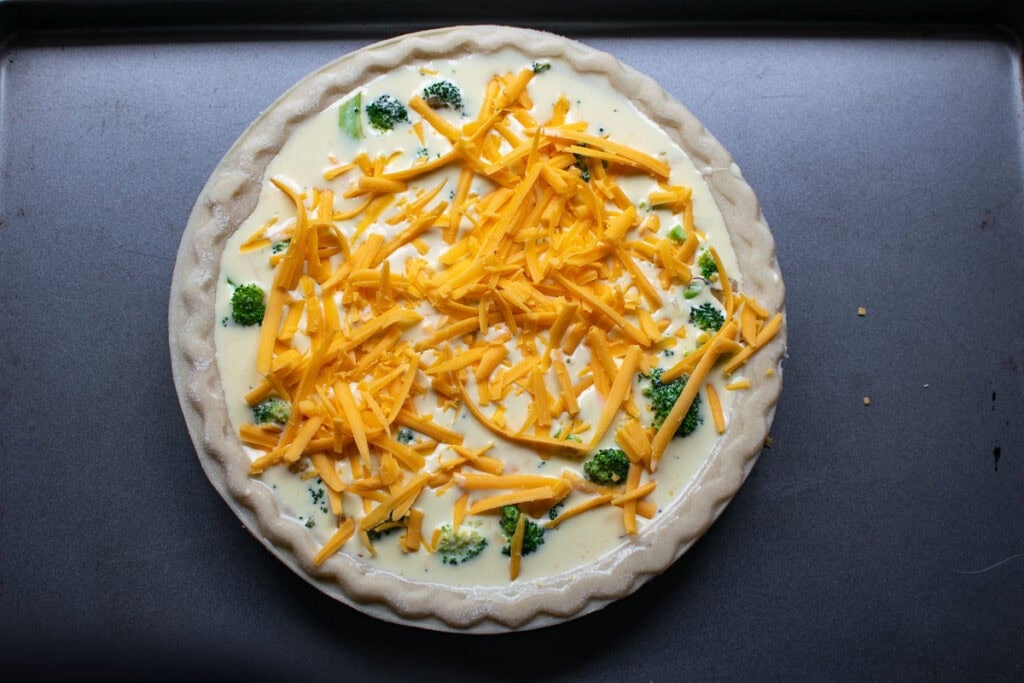 Custard made with eggs, cream and cheddar cheese poured over broccoli in an unbaked pie shell, and sprinkled with extra shredded cheddar cheese.