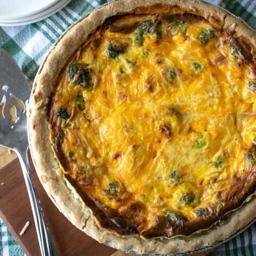 A freshly baked broccoli and cheese quiche on a cutting board with a pie lifter off to the side.
