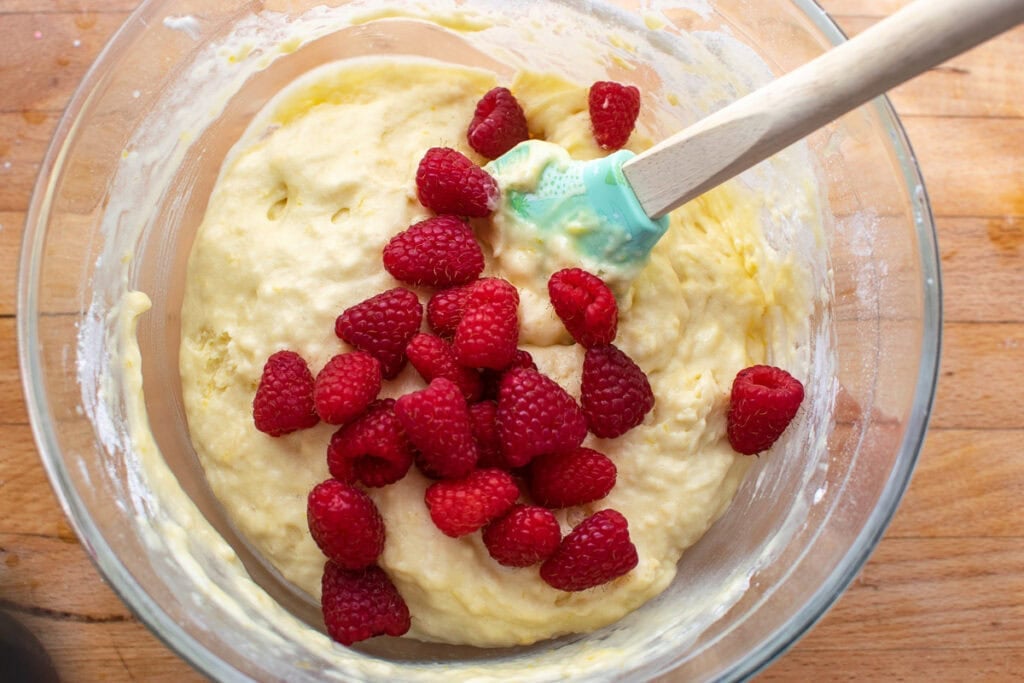 Raspberries added to lemon muffin batter in a large glass mixing bowl before being stirred in.