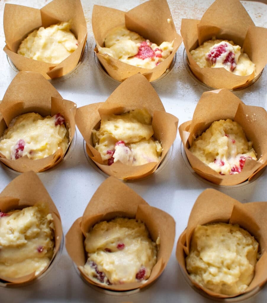 Raspberry lemon muffin batter in a muffin pan lined with tulip shaped muffin liners.