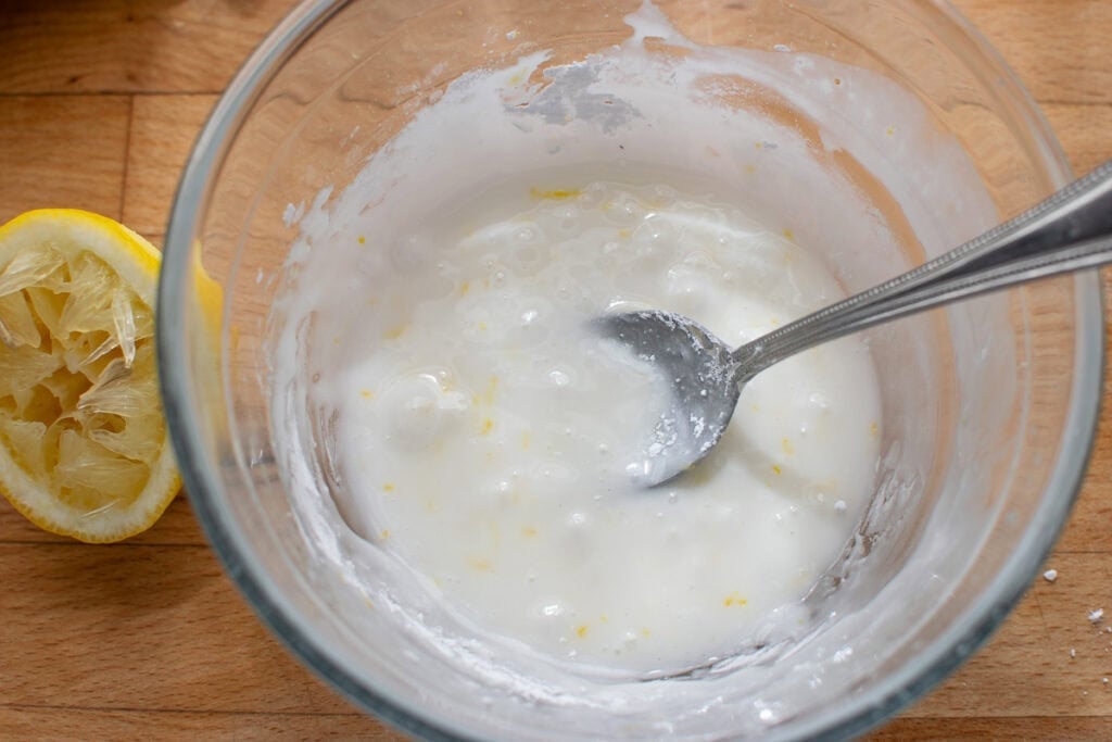 A lemon glaze in a small glass bowl with a spoon in it.