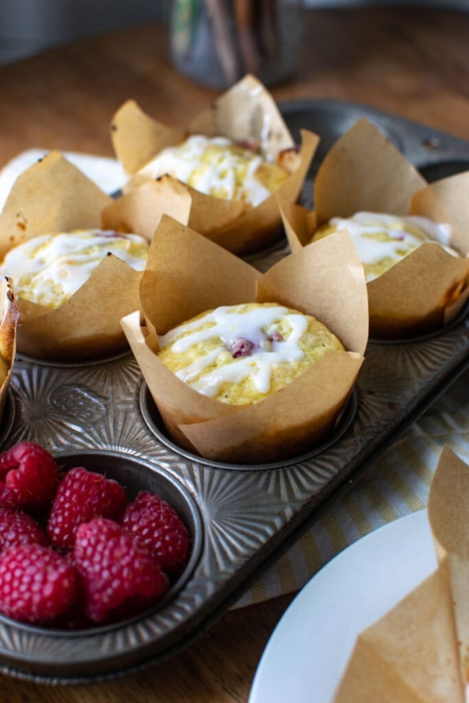 A muffin pan filled with freshly baked lemon raspberry muffins, and one muffin tin filled with fresh raspberries.