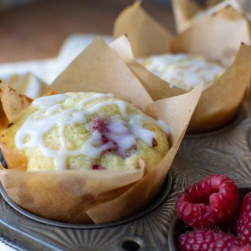 Raspberry lemon muffins in parchment paper muffin liners still in a muffin pan.