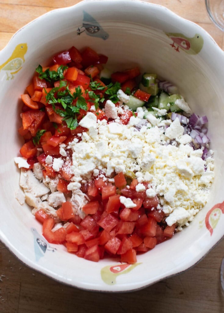All the ingredients for a mediterranean salad with chicken in a large serving bowl before being mixed together.