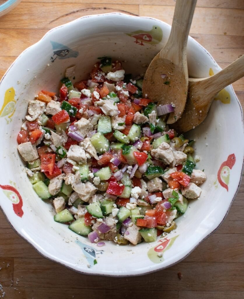 A large mixing bowl filled with chopped veggies, chicken and feta cheese and tossed with a lemon vinaigrette dressing.