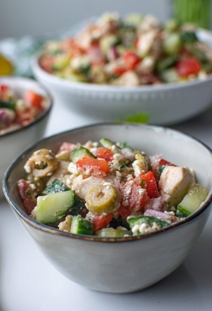 A small bowl of mediterranean salad in the foreground with a large bowl full in the background.