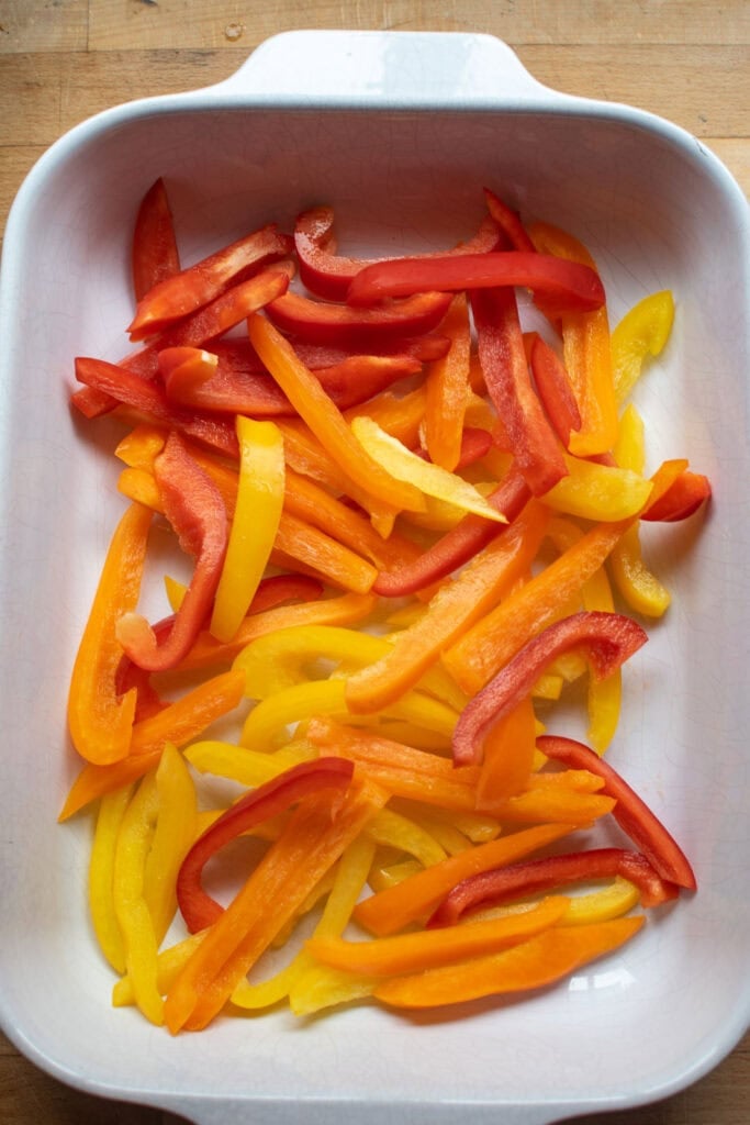 Raw sliced red, orange and yellow bell peppers in a casserole dish.