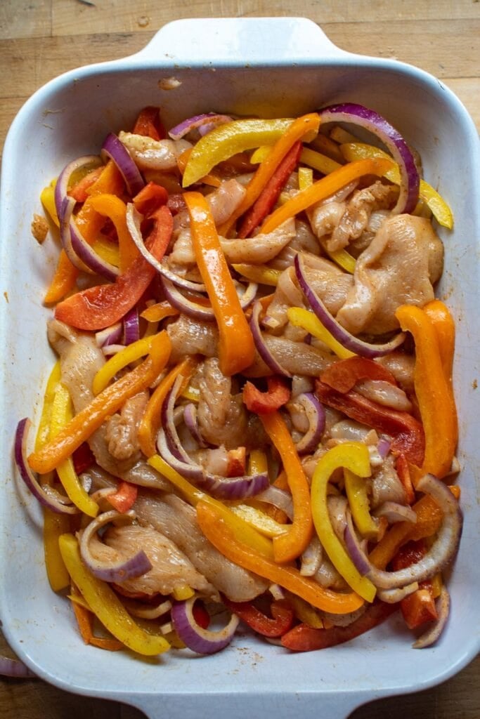 Raw ingredients to make sheet pan chicken fajitas tossed together with fajita seasoning mix and olive oil.