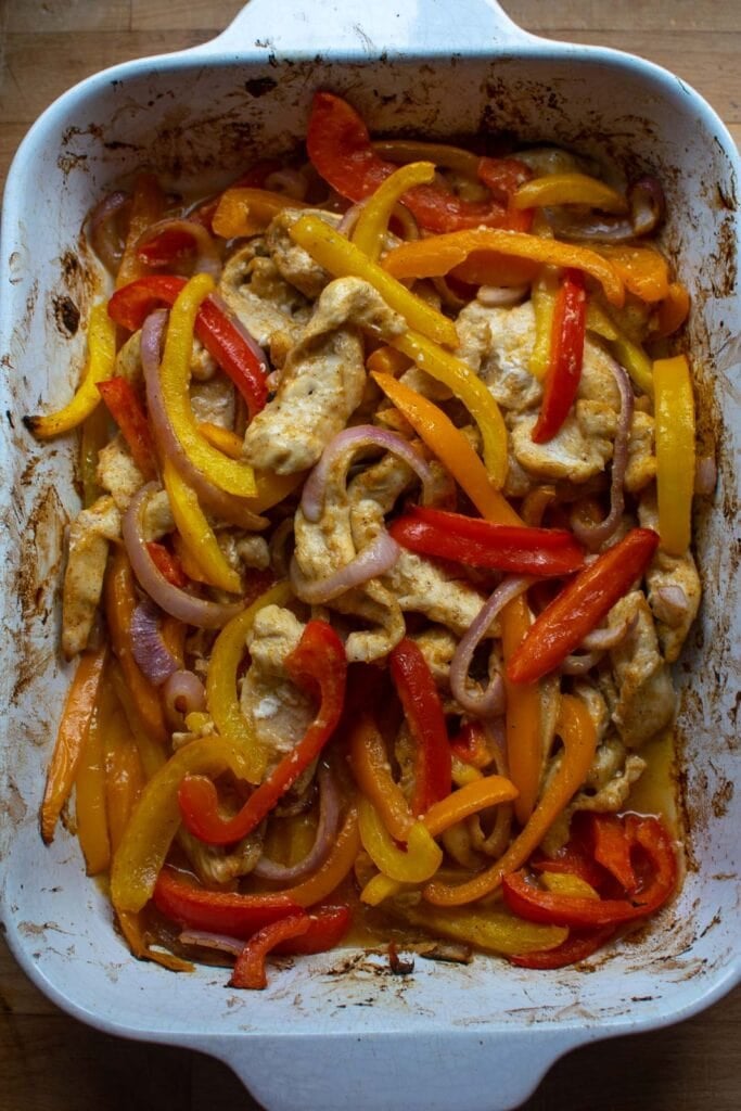 Freshly baked oven chicken fajita mixture including chicken strips, sliced bell pepper and red onion.