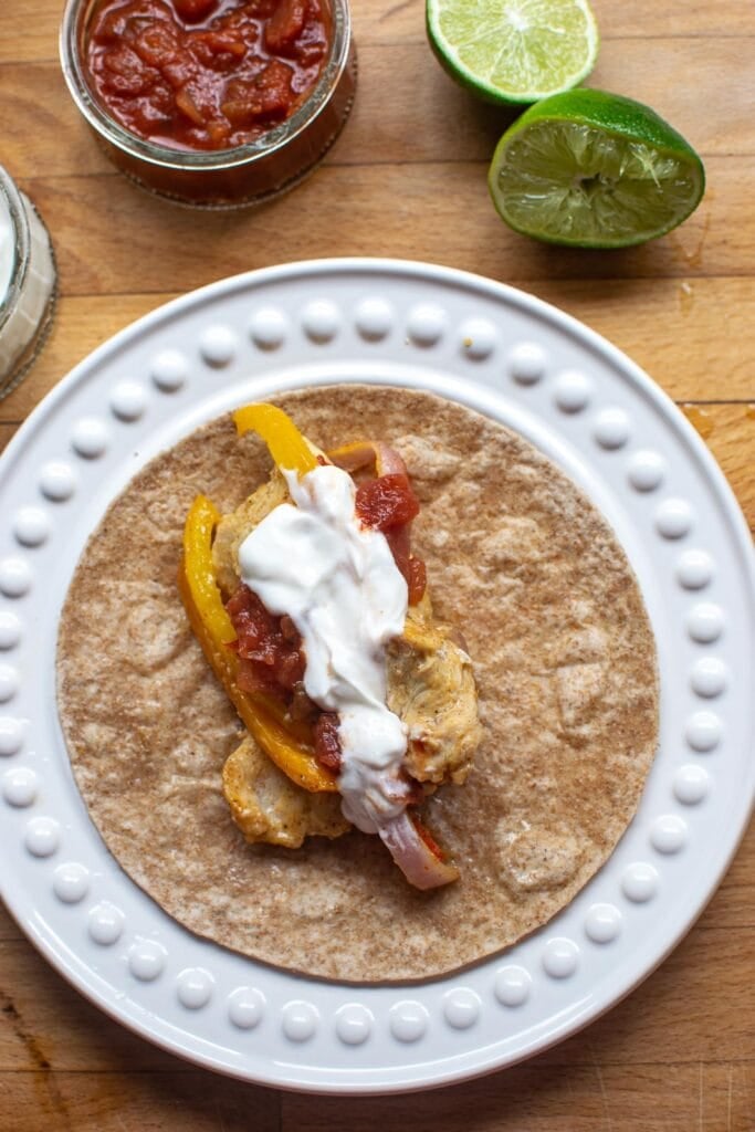 A whole wheat tortilla with a scoop of chicken fajita filling, sour cream and salsa before wrapping it up.