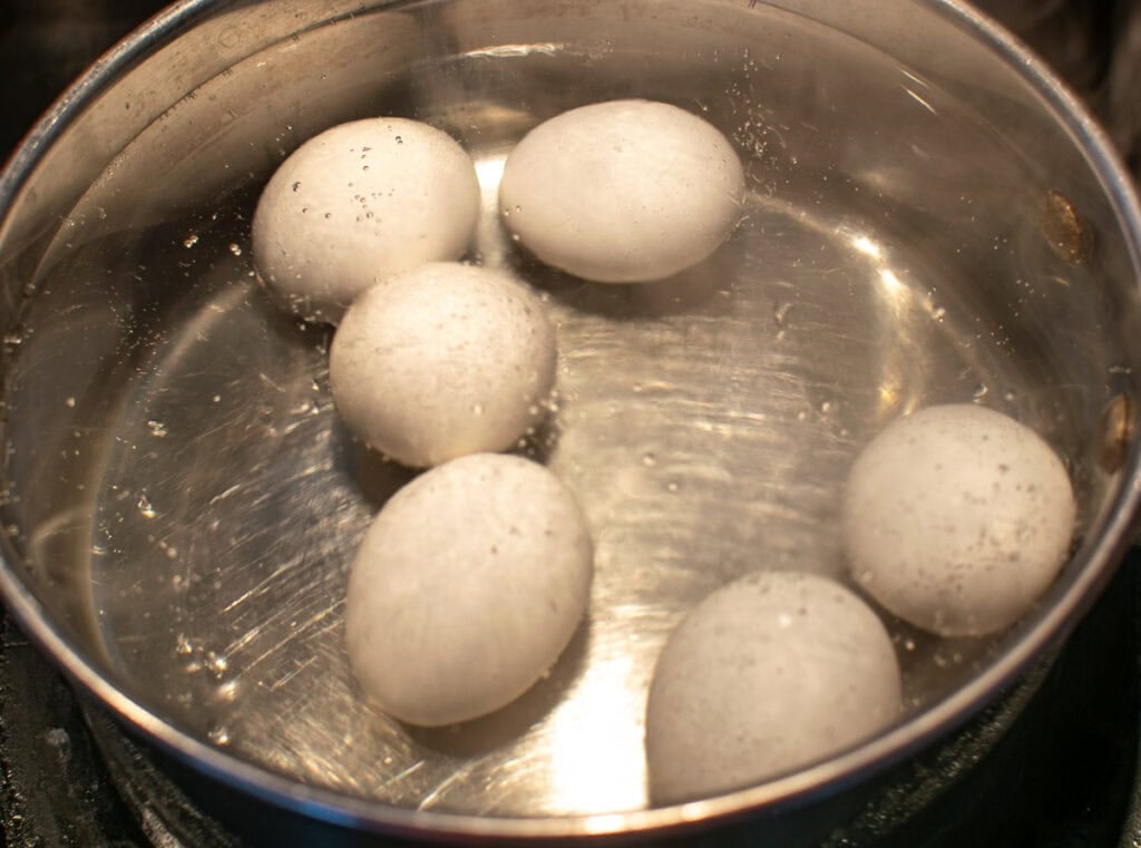Six eggs in a pan of simmering water on the stove top.