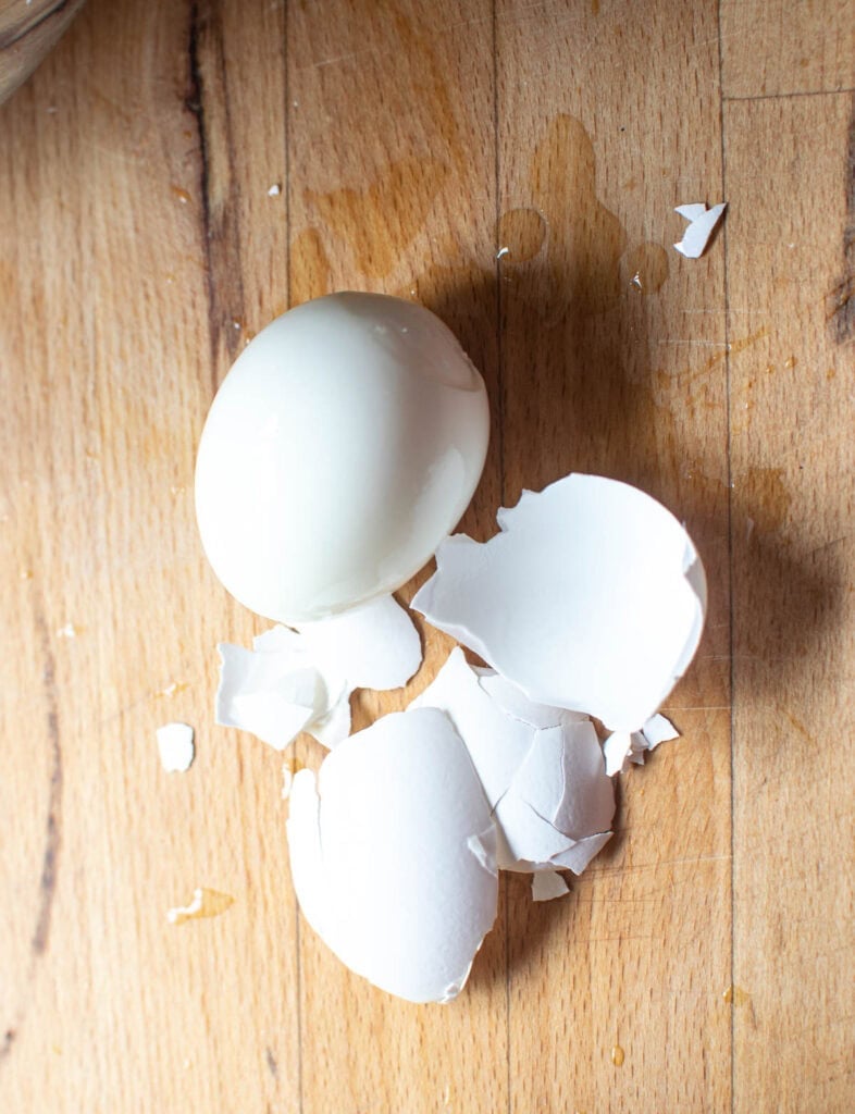 A freshly peeled hard boiled eggs, with the shell beside it.