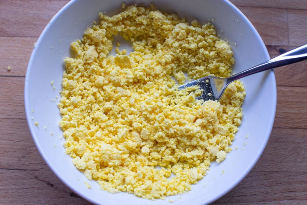 Hard boiled egg yolks that have been mashed with a fork that's still in the bowl.