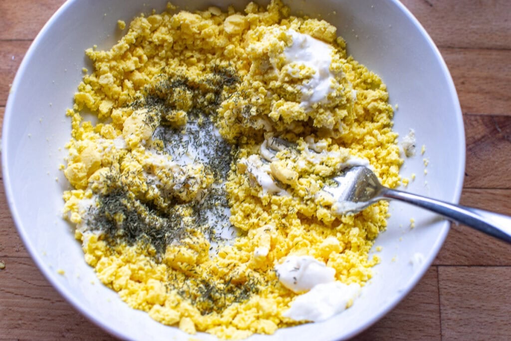 Dill flavoured humus, mayonnaise and dried dill added to a bowl with mashed hard boiled egg yolks.