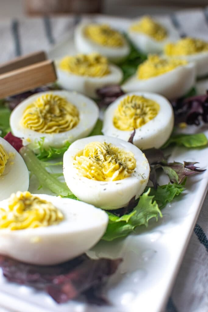 A platter of dill deviled eggs on a bed of lettuce on glass plate.