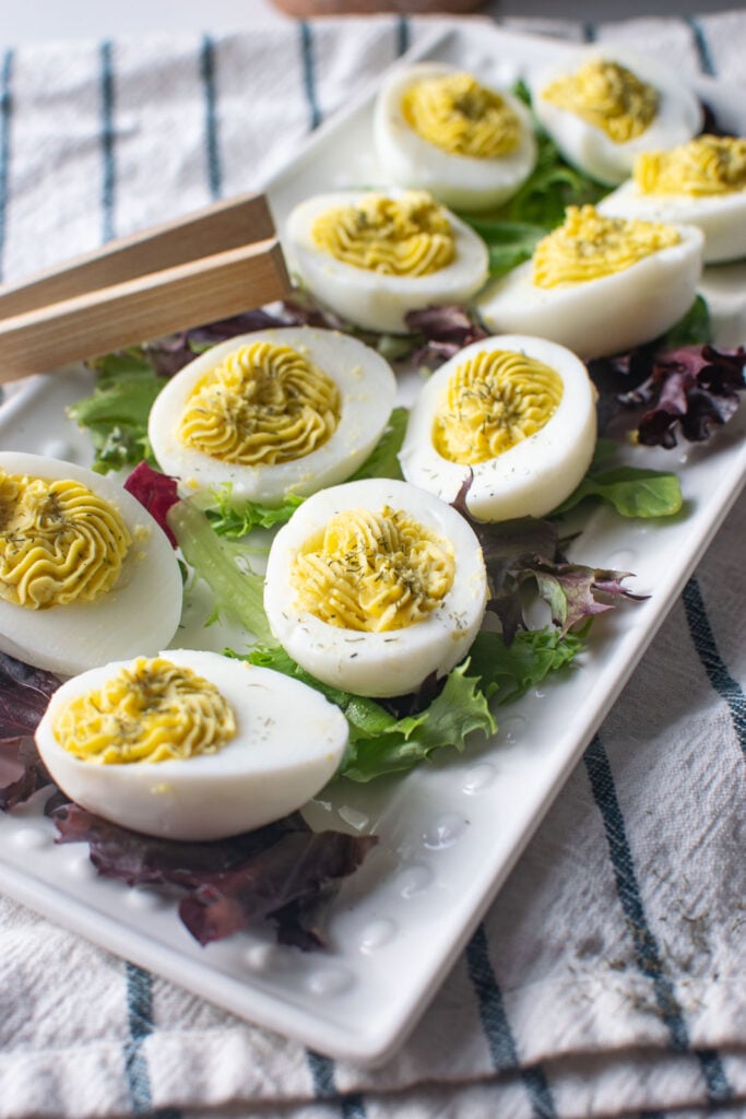 A platter of dill deviled eggs on a bed of lettuce.