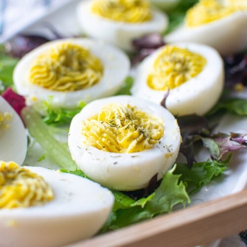 A tray of hard boiled eggs with a dill egg yolk filling piped into the egg white with a star shaped tip.