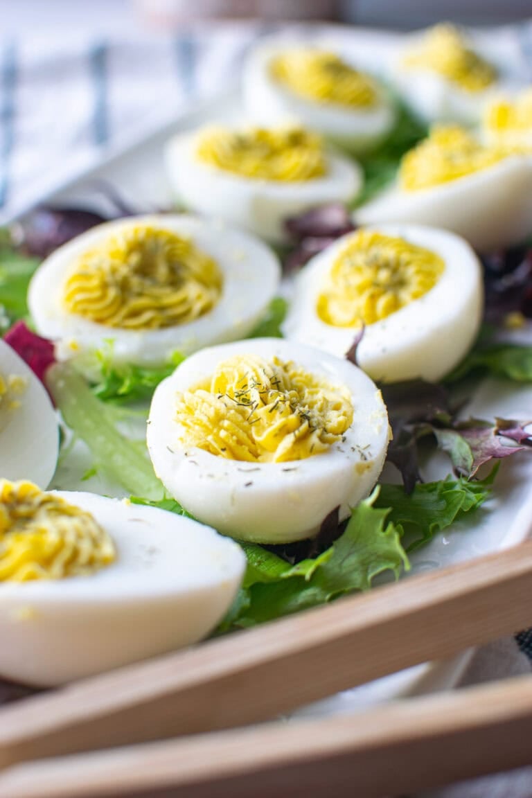 A tray of hard boiled eggs with a dill egg yolk filling piped into the egg white with a star shaped tip.