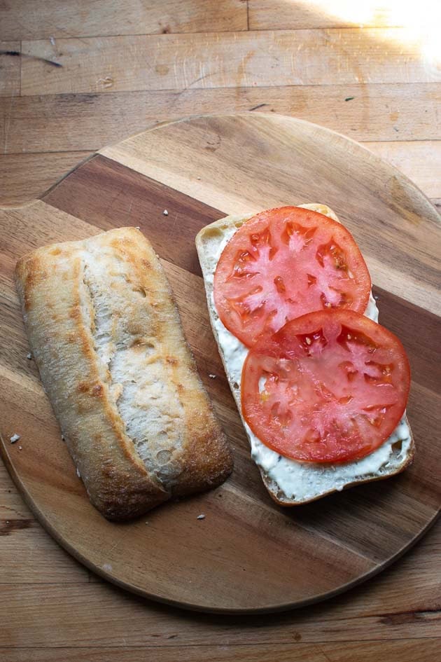 Sliced tomato placed over tarter sauce on the bottom half of a split ciabatta bun.