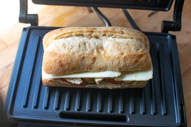 Chicken panini sandwich placed on a hot panini press before pressing.