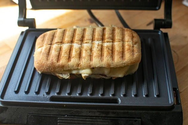 A chicken panini sandwich on a hot panini press after pressing.