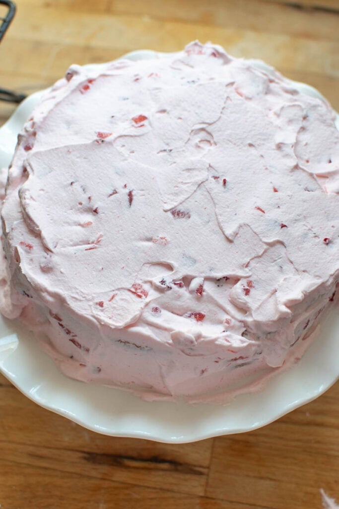 Bottom layer of a 2 tier cake fully frosted in fresh strawberry whipped cream.