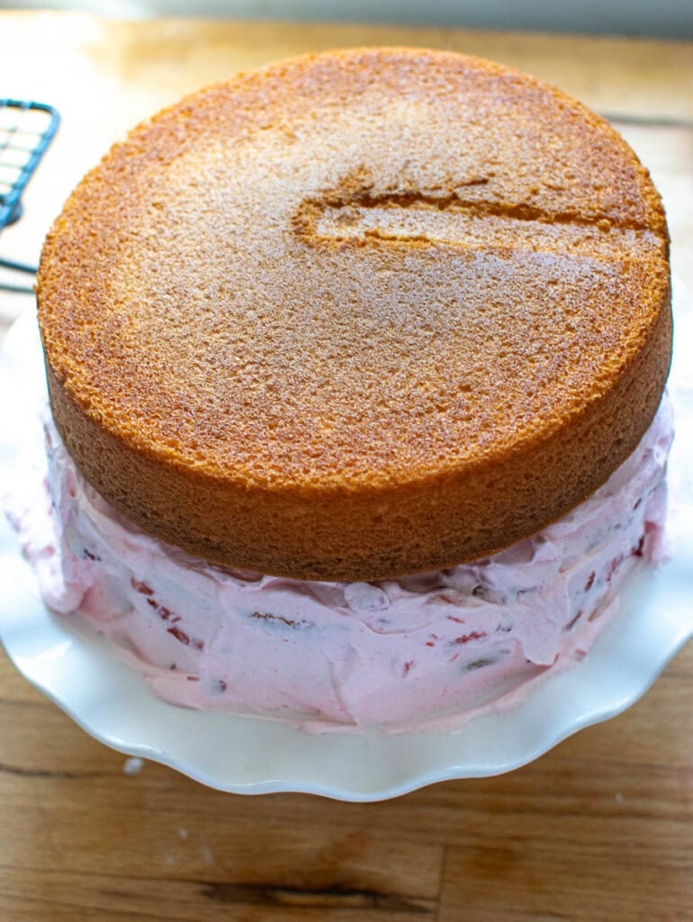 Bottom layer of cake fully covered in strawberry whipped cream frosting and the second unfrosted layer on top.