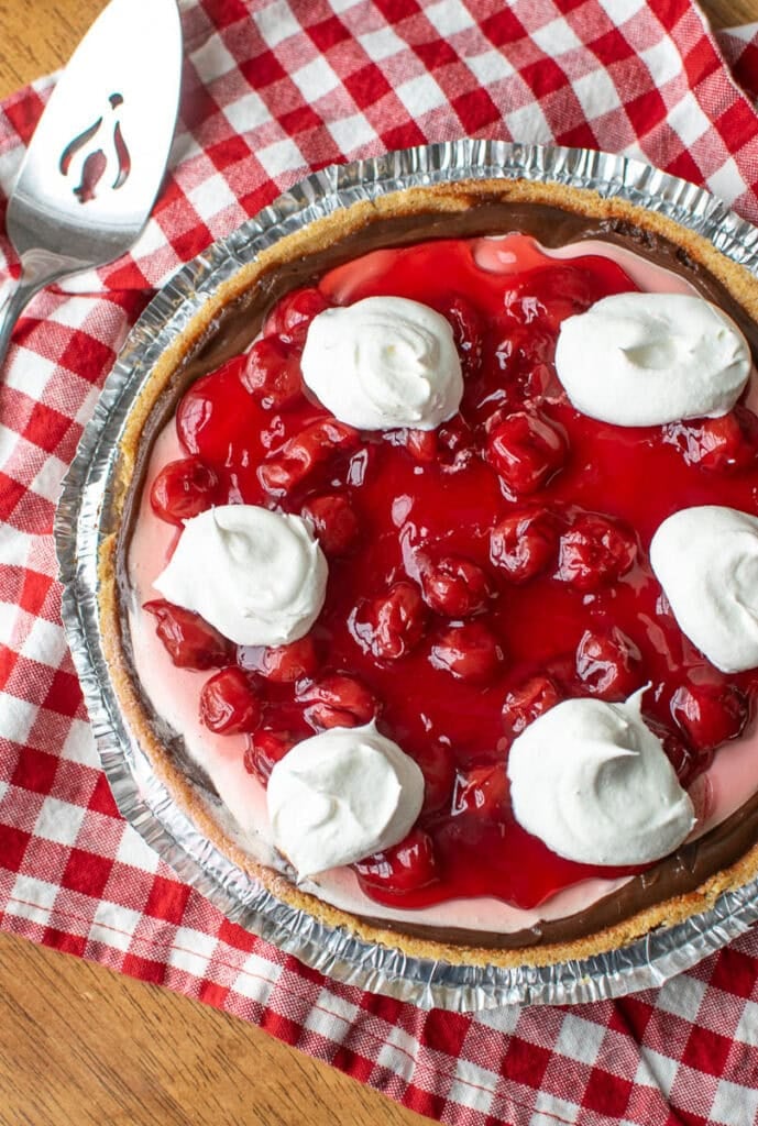 A chocolate cherry no-bake pie in a graham cracker crust garnished with dollops of whipped topping.