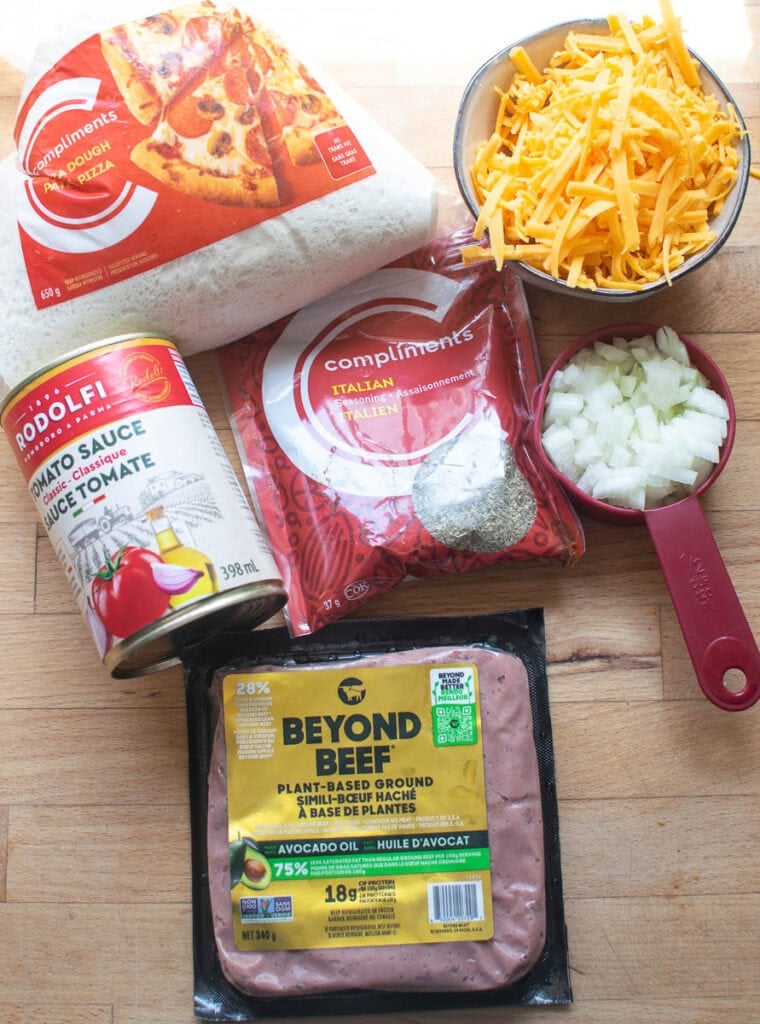 Ingredients to make cheeseburger hand pies including pizza dough, tomato sauce, Italian seasoning, ground beef , cheddar cheese and chopped onion.