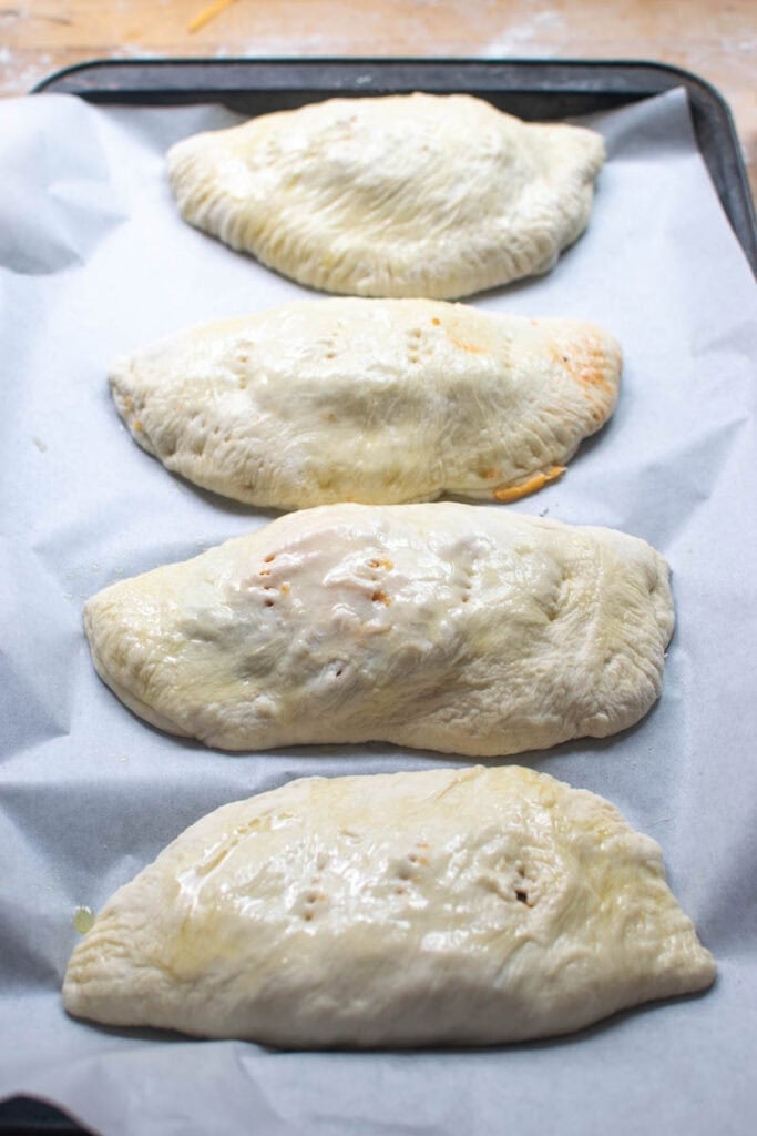 Unbaked cheeseburger hand pies and a parchment lined baking sheet that are brushed with an egg wash, before baking.