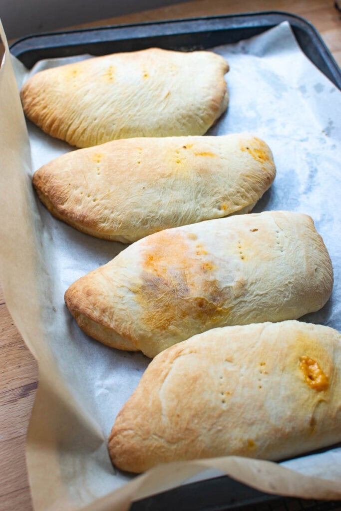 Freshly baked cheeseburger hand pies still on a parchment lined baking sheet.