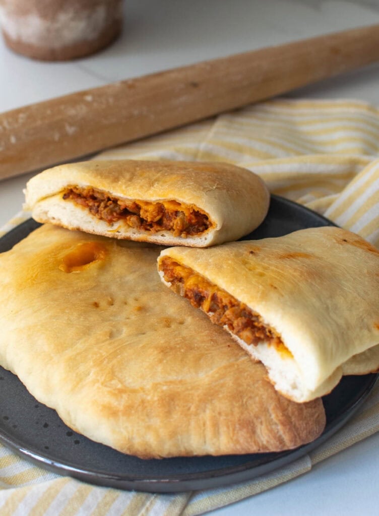 Cheeseburger hand pies made with pizza dough o a plate with one cut in half to show the filling.