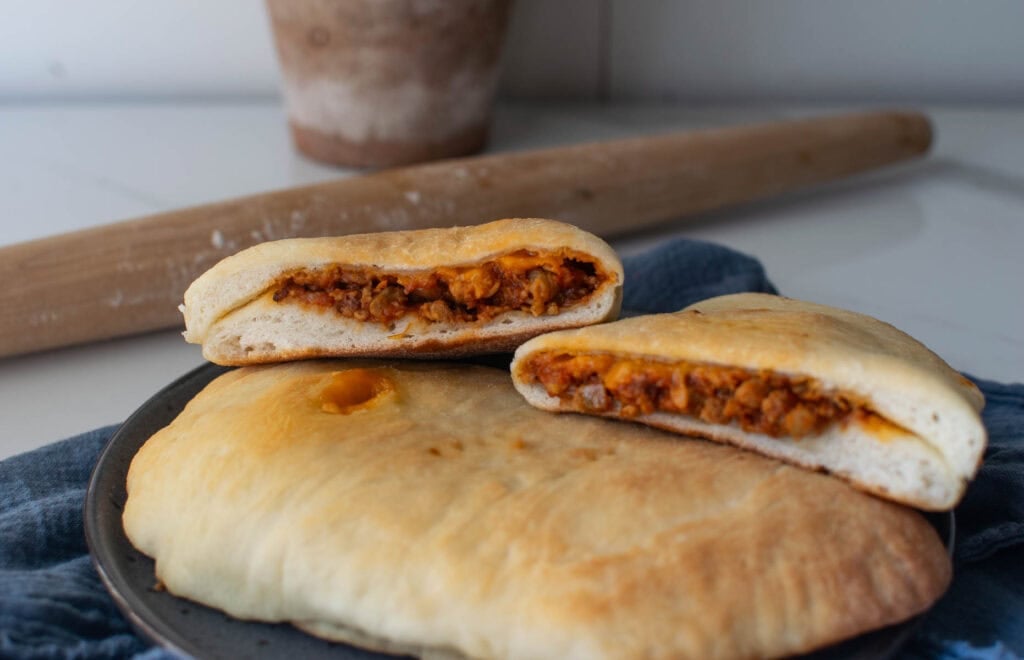 Cheeseburger hand pies on a plate, with the top one cut in half to show the ground beef and cheese filling.