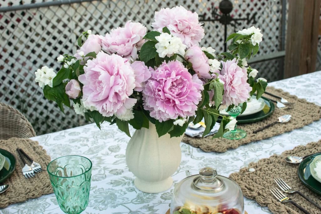 A centrepiece on a summer outdoor dining table made with fresh cut pink peonies and blooming mock orange branches.