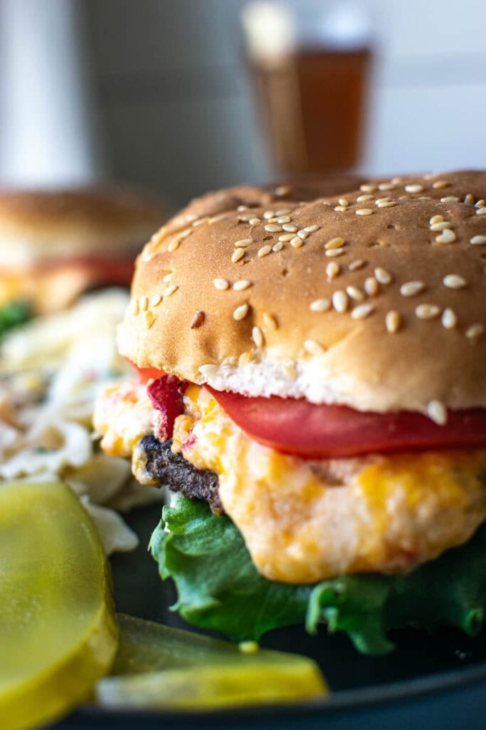 A pimento cheese burger with cheese melting down the sides, topped with tomato and lettuce.