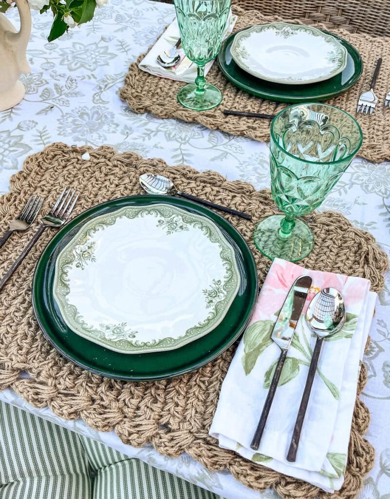 Two place settings including green dinner plates, green floral salad places, napkins with a hint of pink on an outdoor table for a summer gathering.