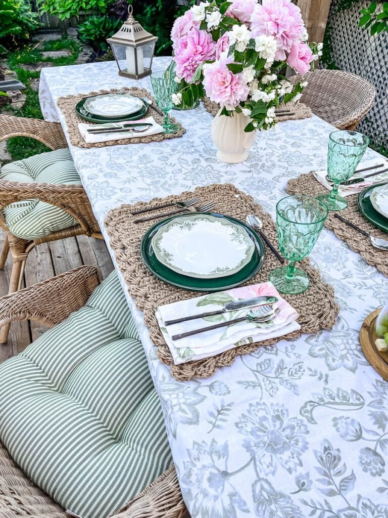 An outdoor table set for a summer gathering with comfortable cushions on the chairs, green dinnerware and pink and green centrepiece.