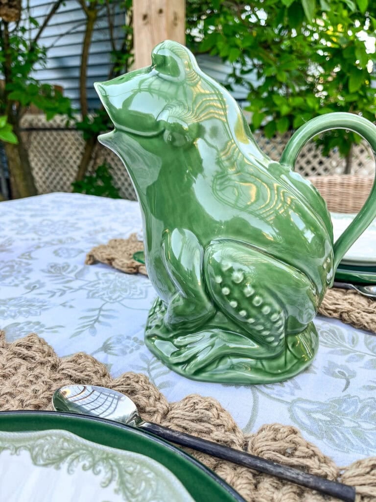 A green frog pitcher on an outdoor table set for dinner with friends.