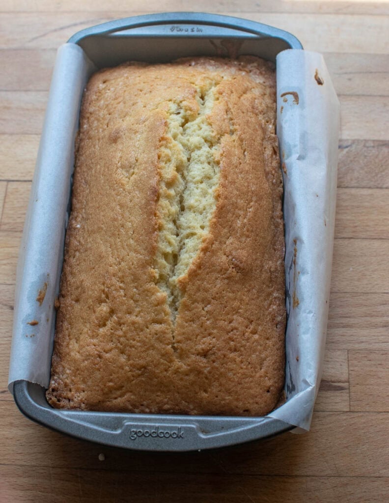 A loaf of freshly baked old-fashioned pound cake in a loaf pan lined with parchment paper.