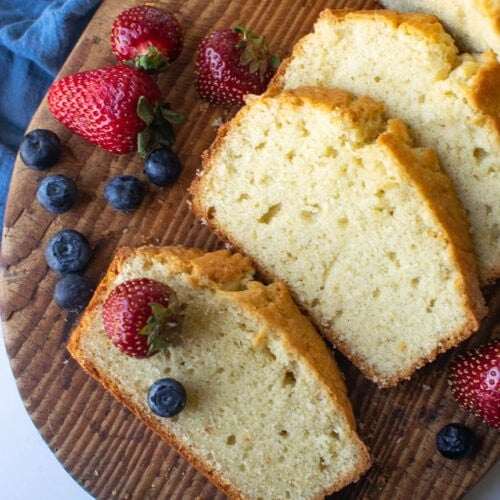 Pound cake on a wood cutting board with 3 slices cut and garnished with strawberries and blueberries.