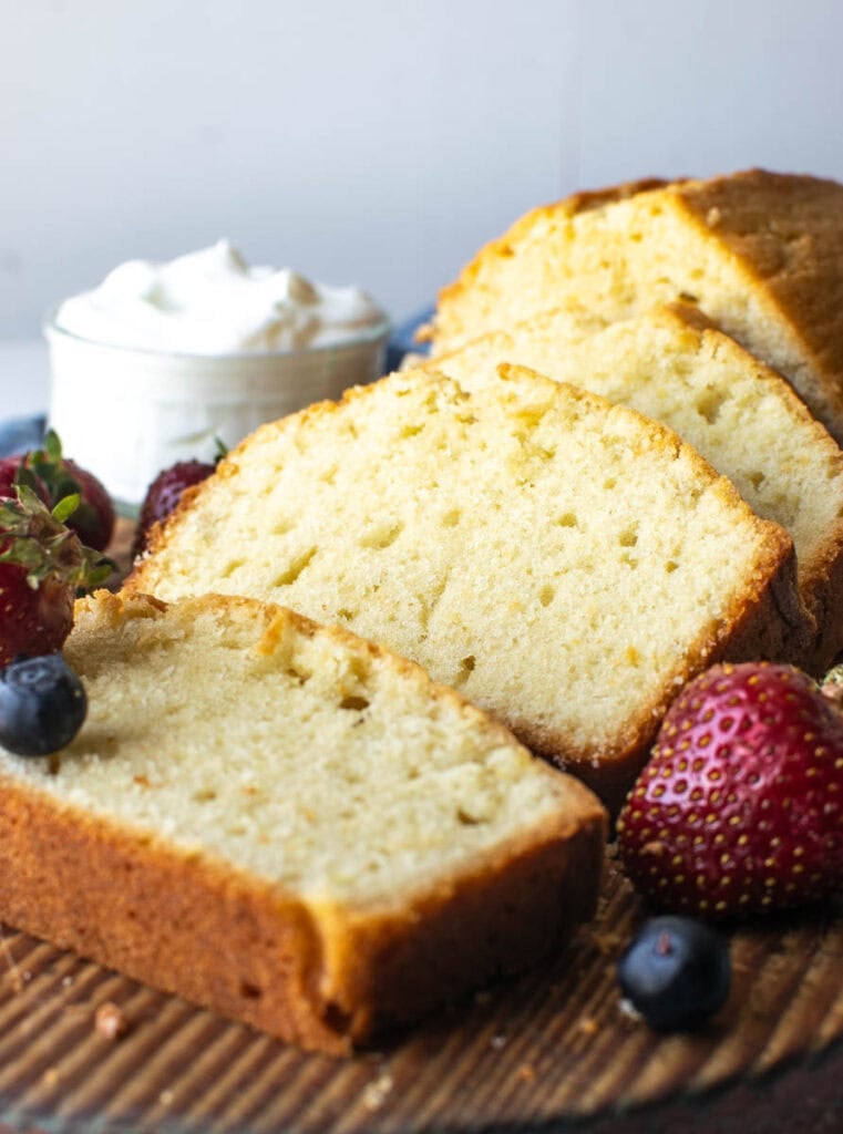 Pound cake on a wood cutting board with a few slices cut and garnished with fresh berries.