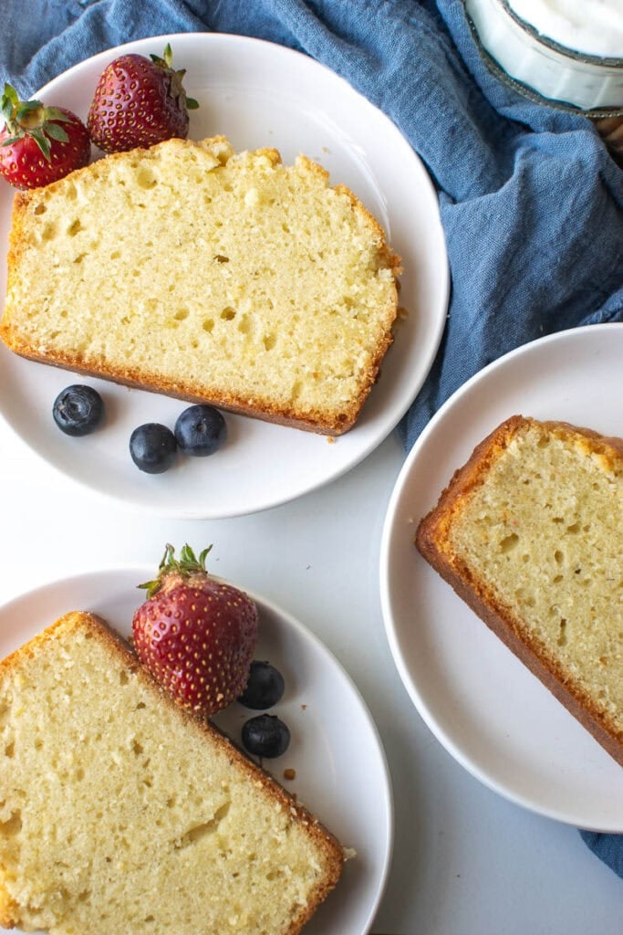 Three slices of classic pound cake on white plates garnished with fresh fruit.