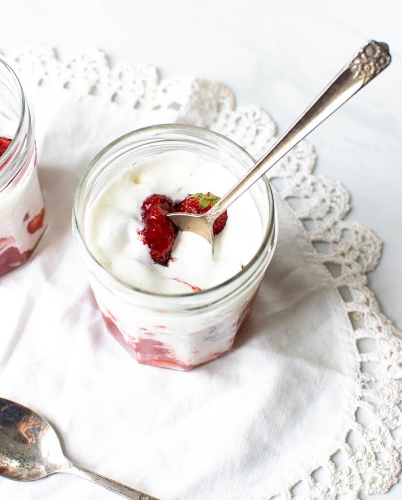 Strawberries and cream in a glass jar with a spoon swirling it.