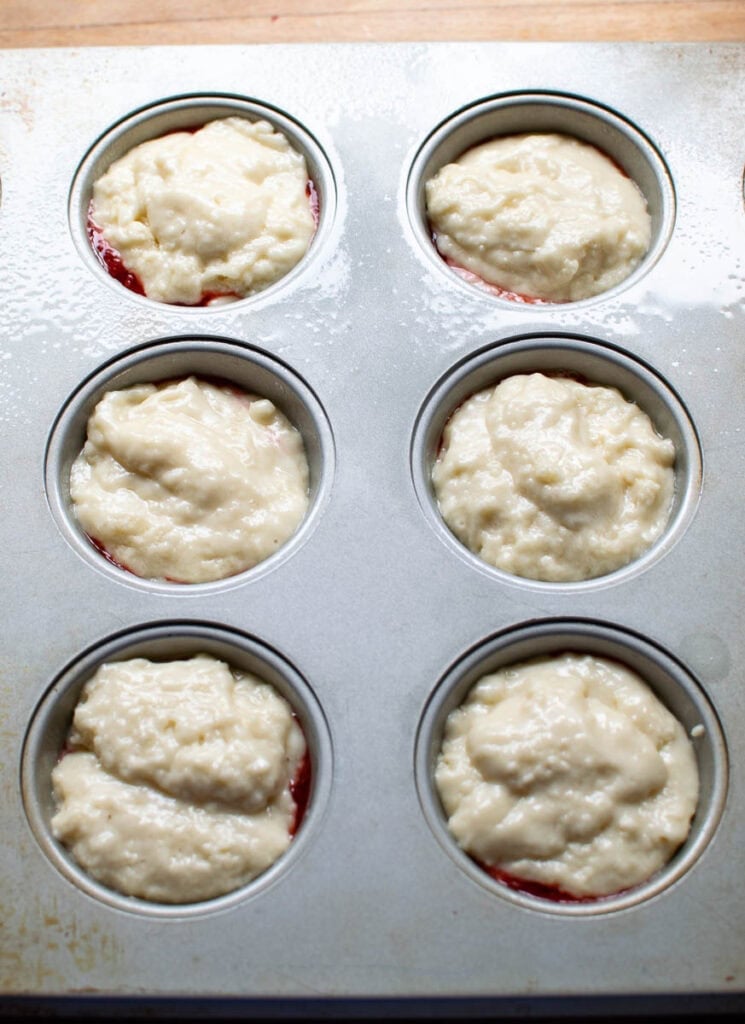 Muffin tins filled with batter with strawberry sauce in the middle.